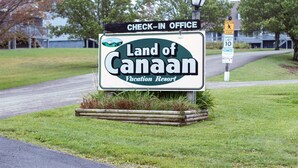 Cartel del Resort Vacacional Land of Canaan, con una oficina de recepción, señal de límite de velocidad y advertencia por cruce de peatones.
