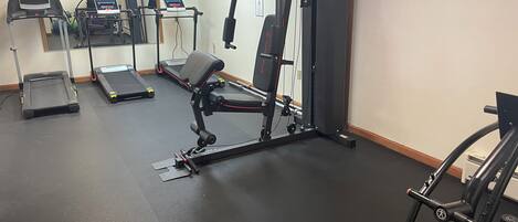 Un gimnasio con cintas de correr, máquinas de pesas y un espejo.