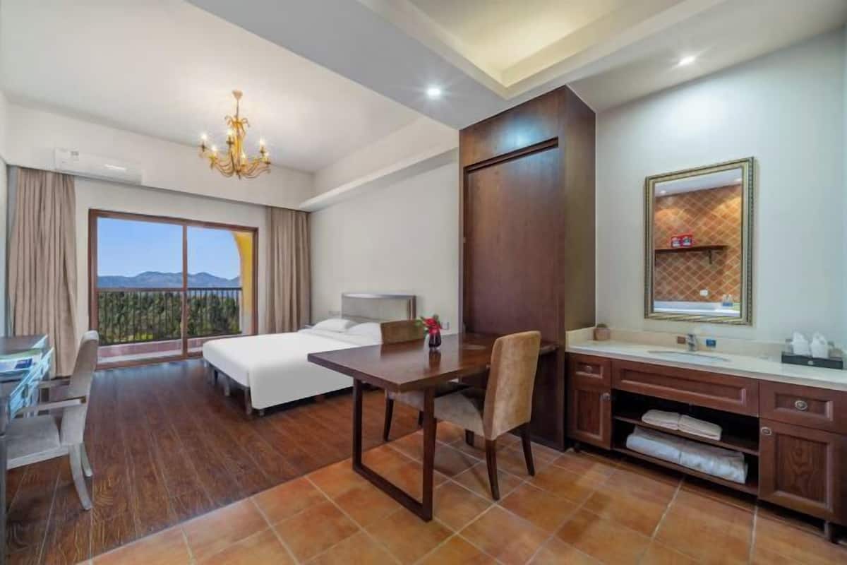 A hotel room with a bed, desk, chair, and a large window with a view.