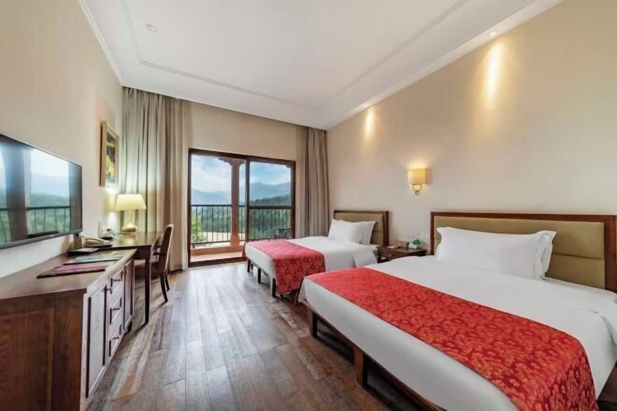 A hotel room with two beds, a desk, a chair, a TV, and a balcony with a view.