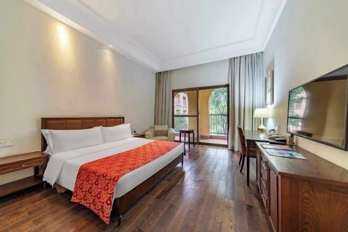 A hotel room with a large bed, a desk, a chair, and a TV.