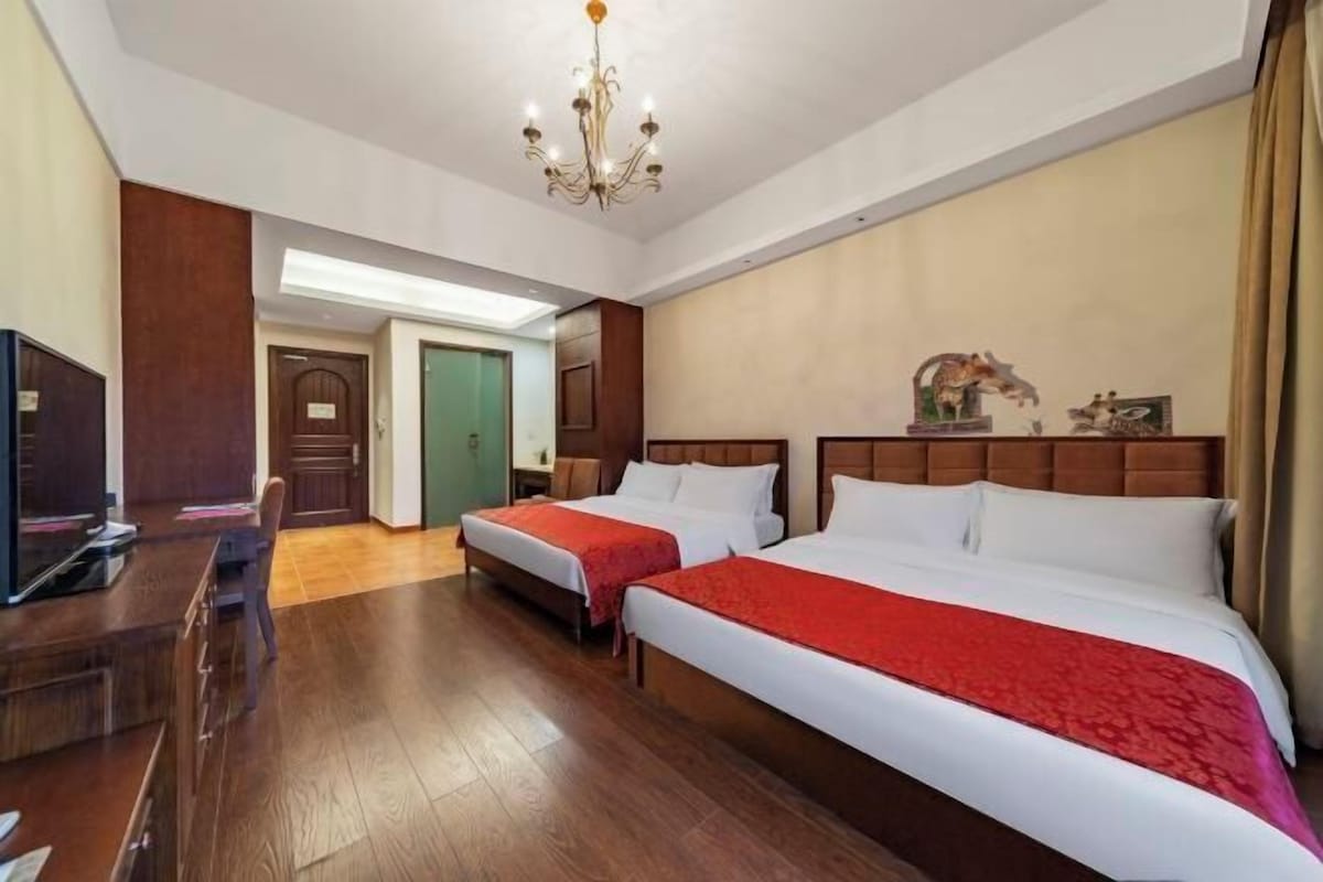 Habitación de hotel con dos camas, televisión, piso de madera y candelabro.