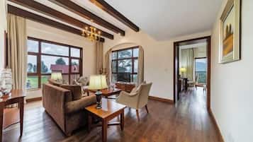 A room with wooden flooring, a sofa, a table, a lamp, and large windows with a view of trees and buildings.