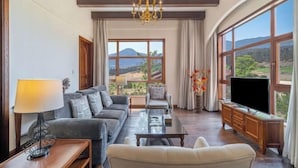 Sala de estar com sofá, poltrona, mesa de centro, TV e grandes janelas com vista para as montanhas.