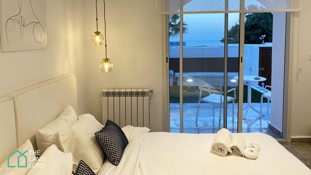 A bedroom with a bed, pillows, a radiator, and a view of an outdoor patio with a table and chairs. - New 1 bd With Garden and sea Side at Marsa Cornich (La Marsa)
