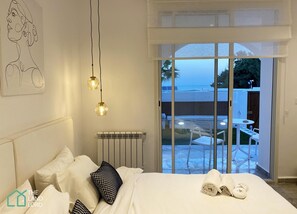 A bedroom with a bed, pillows, a radiator, and a view of an outdoor patio with a table and chairs. - New 1 bd With Garden and sea Side at Marsa Cornich (La Marsa)