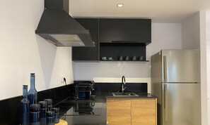 Une cuisine moderne avec des meubles noirs, un réfrigérateur en acier inoxydable, un plan de travail en bois et une hotte aspirante noire.