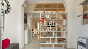 Un intérieur moderne avec une bibliothèque blanche, un coussin rouge en forme de cœur et un panneau décoratif portant l’inscription « HOME » sur le mur.
