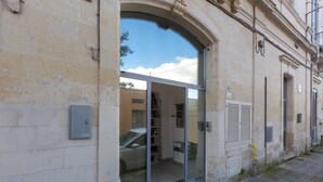 Un bâtiment doté d’une grande porte d’entrée en verre, avec une voiture garée devant, et dont l’intérieur est visible, avec des étagères et une petite table.
