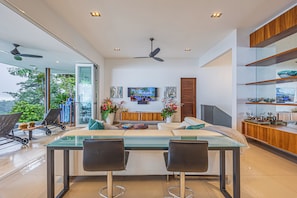 A modern living room with a glass dining table, two chairs, a sofa, a TV, and a ceiling fan. - Casa Nandi - Spectacular Ocean Views and Wildlife (Bahia Ballena)
