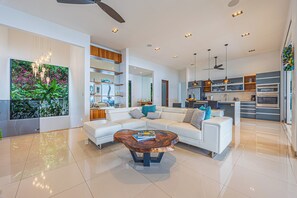 A modern living room with a white sofa, a wooden coffee table, and a large painting of plants.