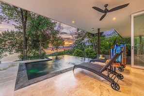 An infinity pool with a view of the sunset, a ceiling fan, and outdoor furniture. - Casa Nandi - Spectacular Ocean Views and Wildlife (Bahia Ballena)