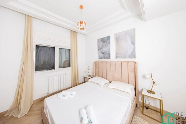 Une chambre à coucher avec un grand lit, deux tables de chevet, un radiateur et une fenêtre avec des rideaux.