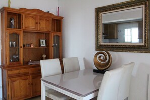 A dining area with a wooden cabinet, a table with chairs, and a large mirror on the wall. - 2 Bed 2 Bath Apt, Huge Corner Plot, Trampoline, Golf, Sun, Good Food (Orihuela Costa)