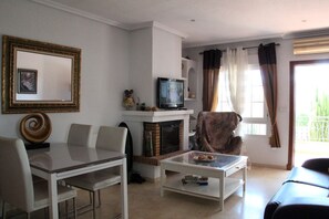 A living room with a television, a fireplace, a dining table, and a sofa. - 2 Bed 2 Bath Apt, Huge Corner Plot, Trampoline, Golf, Sun, Good Food (Orihuela Costa)