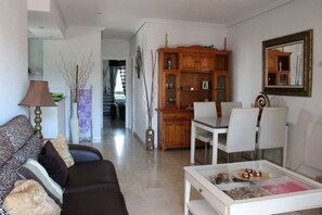 A living room with a sofa, a coffee table, a dining table with chairs, a wooden cabinet, and a mirror on the wall. - 2 Bed 2 Bath Apt, Huge Corner Plot, Trampoline, Golf, Sun, Good Food (Orihuela Costa)