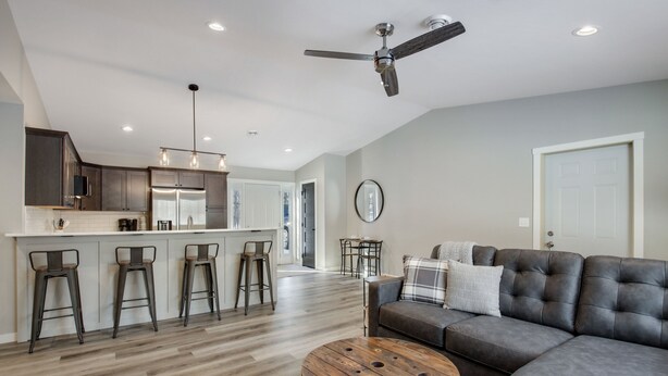 A modern kitchen with a bar area, a dining table, and a living room with a sofa and coffee table. - Up North Living!  Fully renovated one-level living home in wooded lot near lake. (Cumberland)