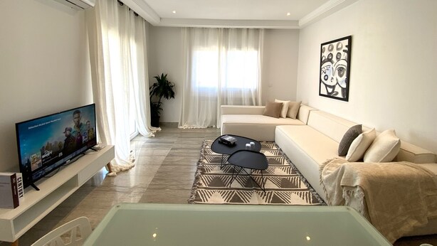 A modern living room with a flat-screen TV, a sofa, a coffee table, and a patterned rug.