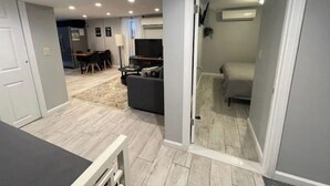 Ein modernes Wohnzimmer mit einer Couch, einem Couchtisch und einem Fernseher. Im Hintergrund ist ein Essbereich mit Stühlen und einem Tisch zu sehen.