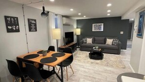 Ein modernes Wohnzimmer mit einem grauen Sofa, einem Couchtisch und einem Essbereich mit einem Holztisch und schwarzen Stühlen.