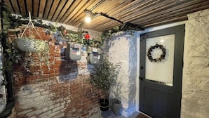 Ein rustikaler Innenraum mit unverputzten Backsteinwänden, Holzbalkendecke und einer Tür mit Adventskranz.