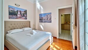 A neatly made bed with a headboard, two wall-mounted paintings, and a wooden floor. - Elegant Apartment in Parliament Square (Athens)