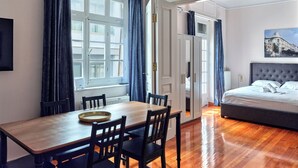 A hotel room with a wooden dining table, chairs, a bed with a grey headboard, and a painting on the wall. - Elegant Apartment in Parliament Square (Athens)