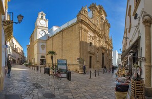 A cobblestone street with historic buildings, a clock tower, and a market stall. - 3158 Sterlizia House by Barbarhouse (Gallipoli)