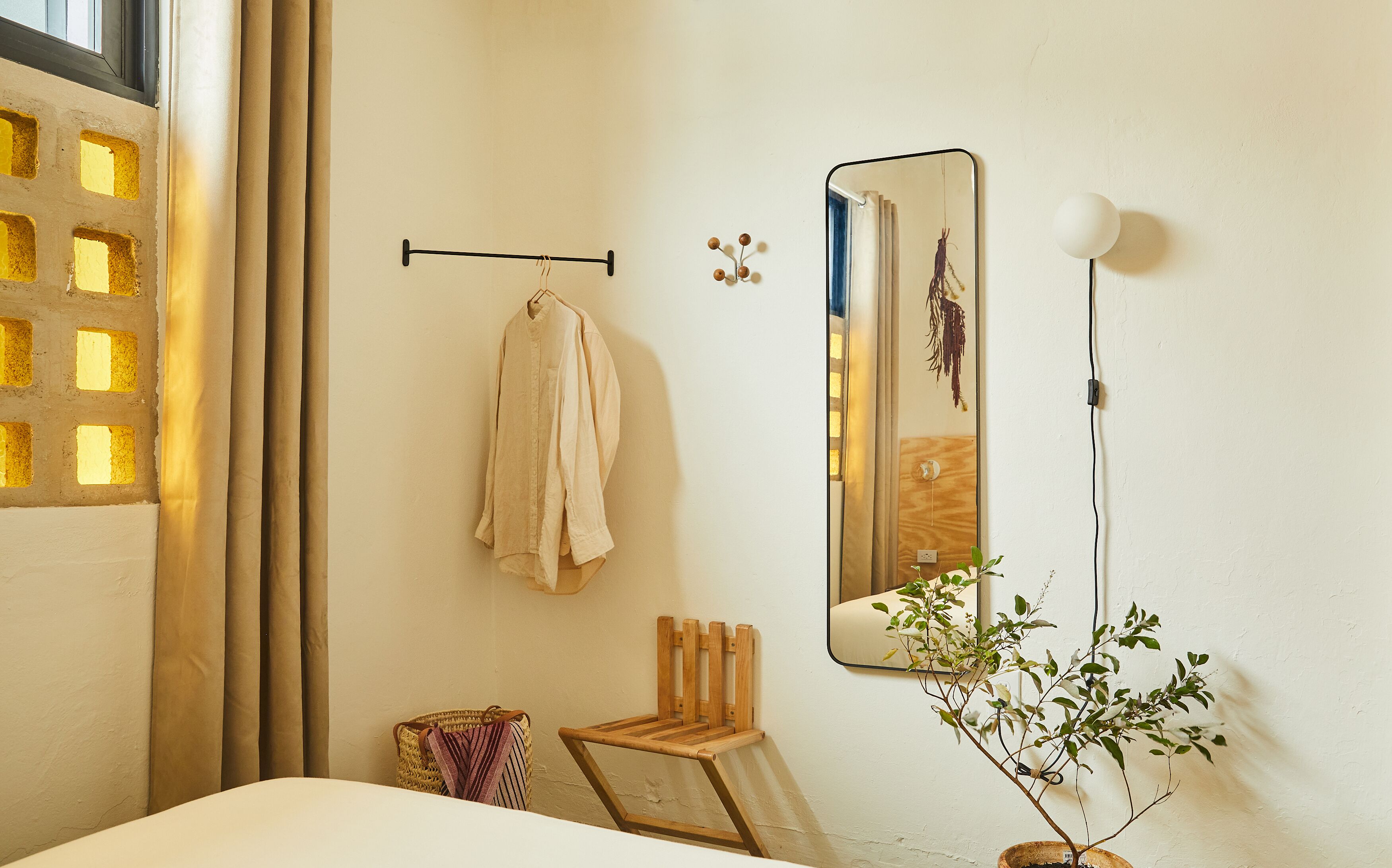 Quarto com cama, cadeira de madeira, mesinha, espelho e planta em vaso.