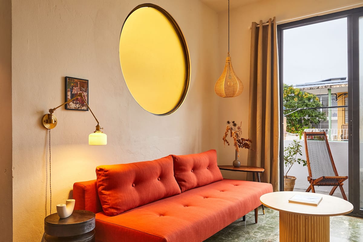 A modern living room with a red sofa, a round table, a hanging light fixture, and a large mirror on the wall.