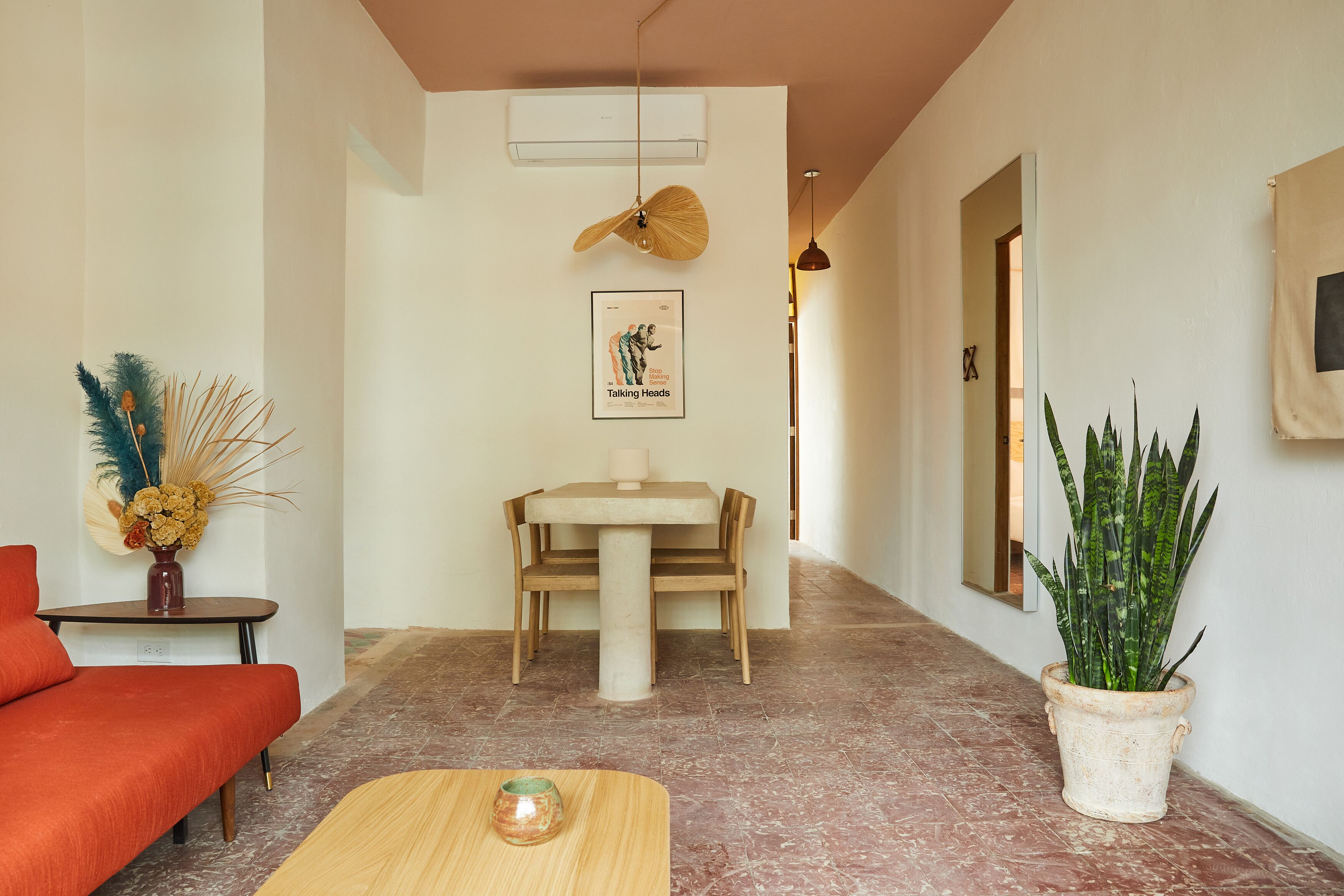 A hallway with a dining table and chairs, a sofa, a potted plant, and a framed picture on the wall.