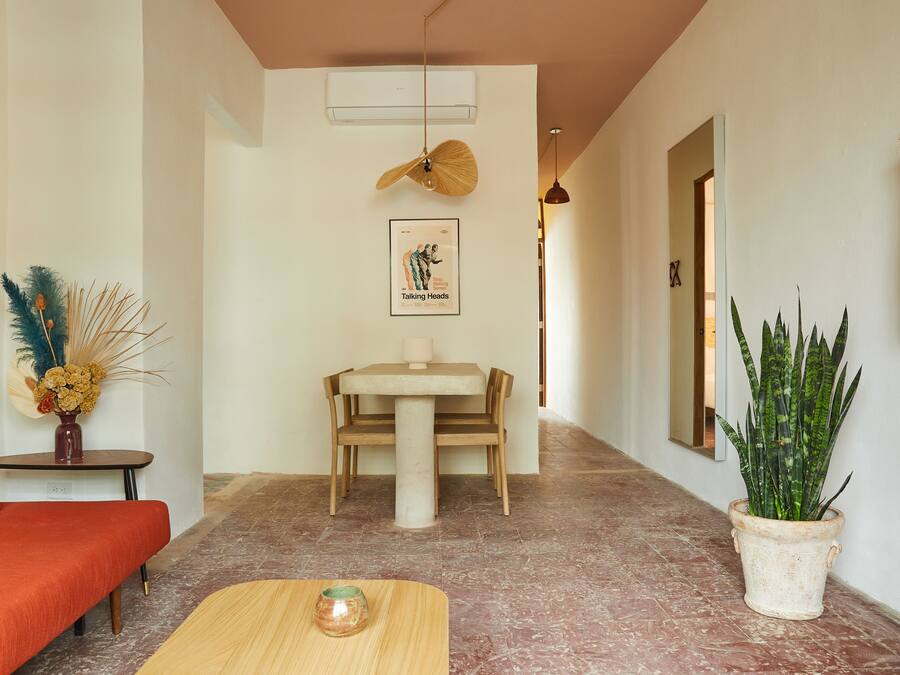 Un couloir comprenant une table à manger et des chaises, un canapé, une plante en pot et un tableau encadré accroché au mur.