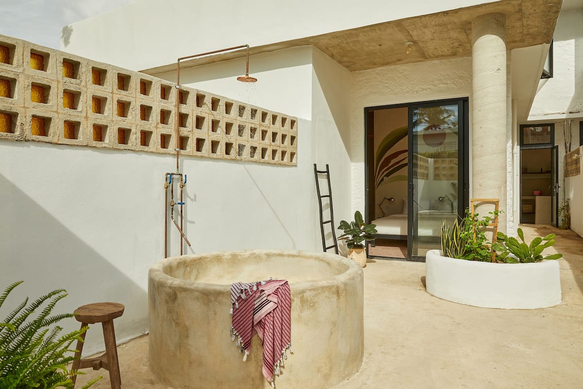 A modern outdoor area with a concrete water feature, a wooden stool, and a planter with plants.