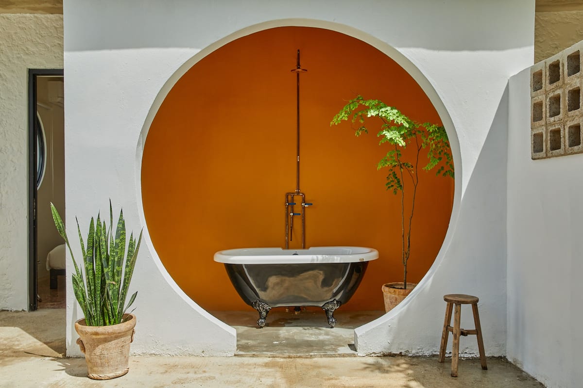 A bathtub in a circular alcove with a white wall and an orange backdrop.