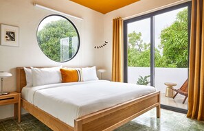 A bedroom with a large bed, a round window, and a view of greenery outside. - APT by DW (San Juan)