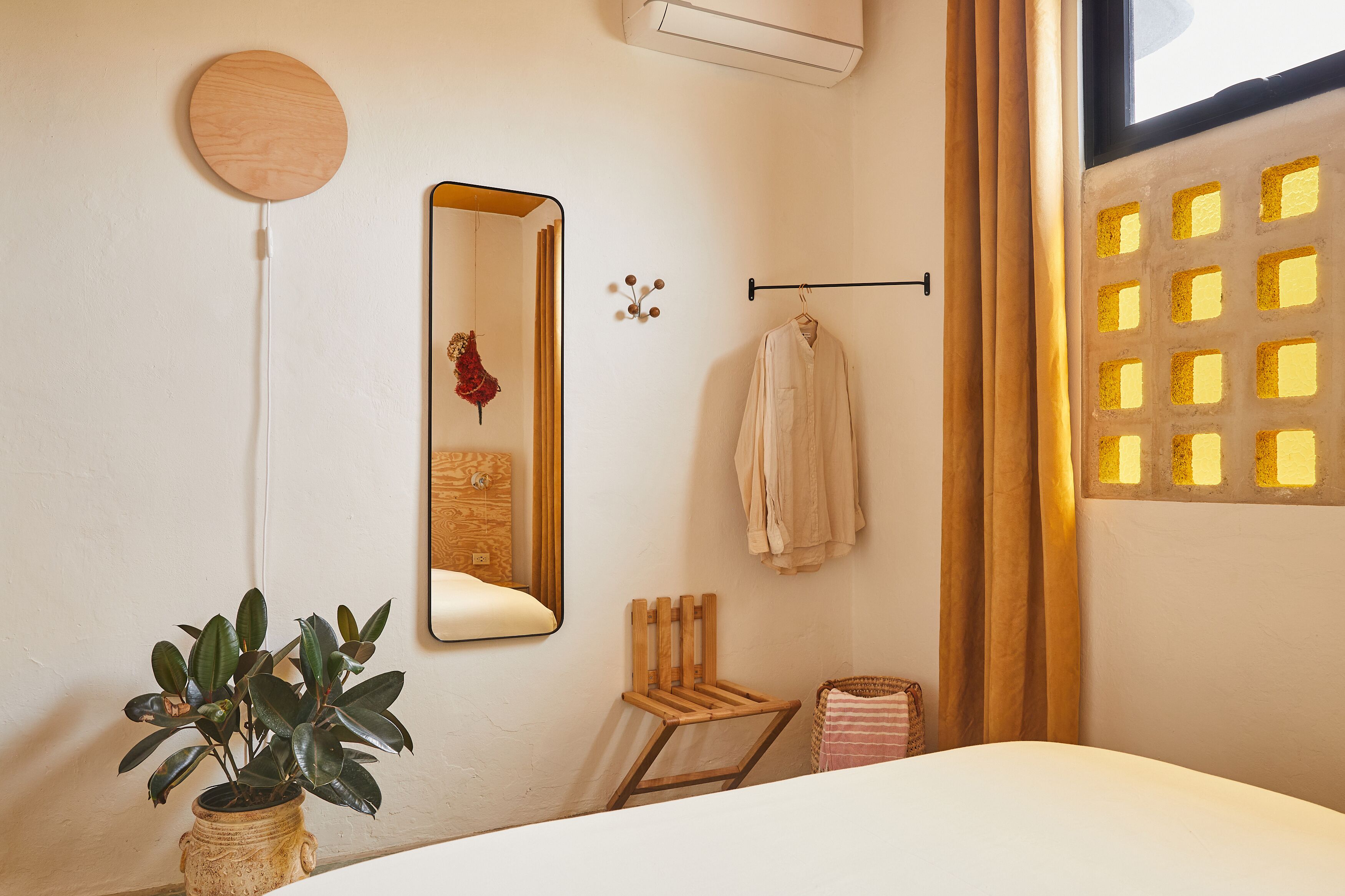 Habitación de hotel con cama, planta en maceta, espejo, toallero y ventana con vistas.
