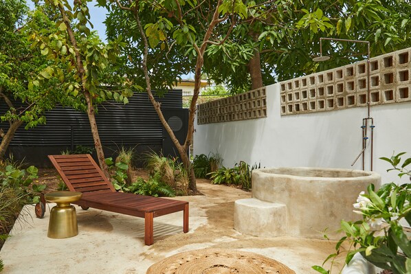 A patio with a wooden lounge chair, a concrete planter, and a small table. - APT by DW (San Juan)
