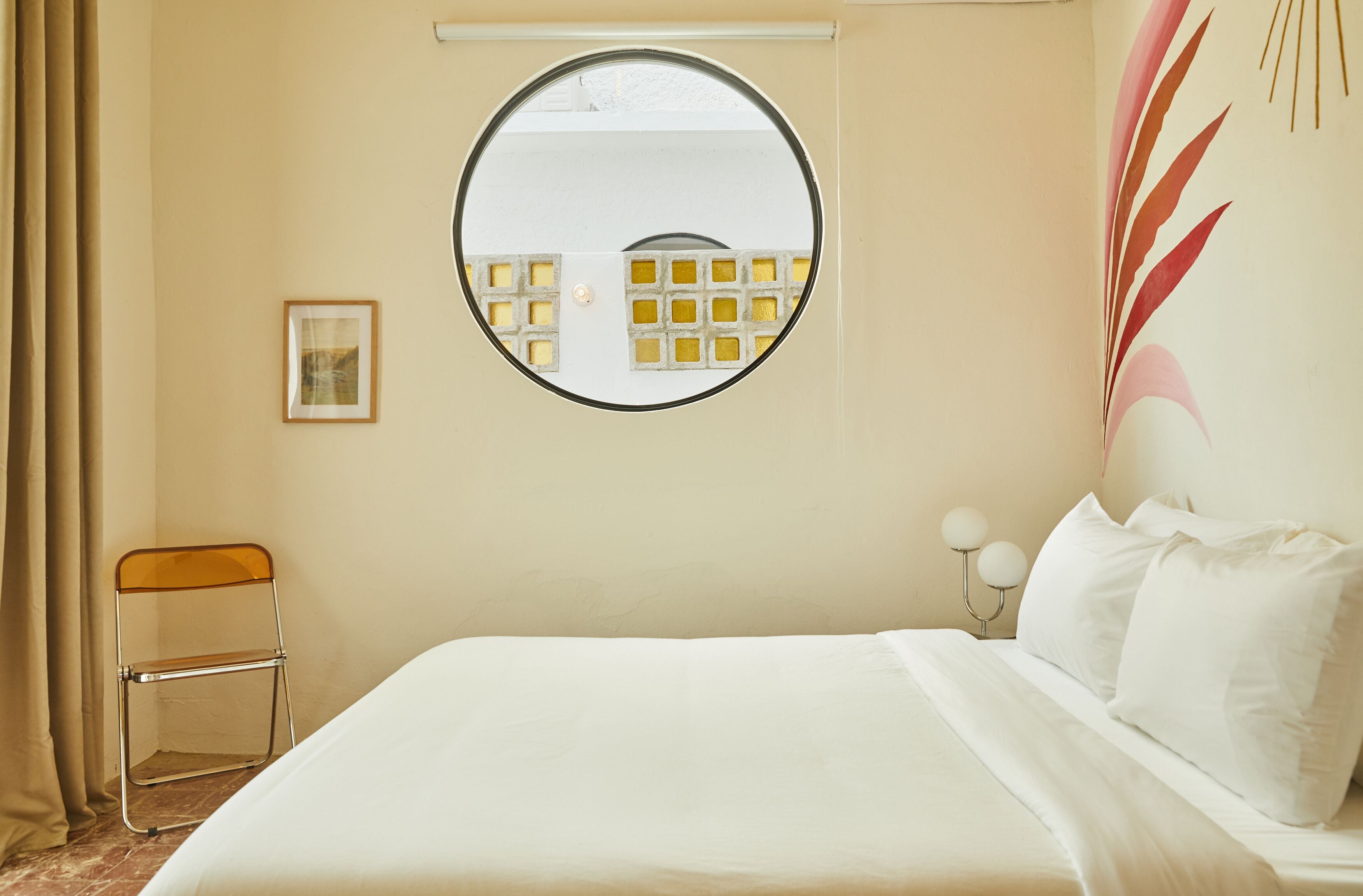 A hotel room with a bed, a round mirror, a chair, and a picture on the wall.