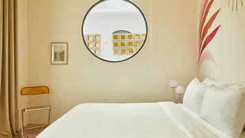 A hotel room with a bed, a round mirror, a chair, and a picture on the wall.