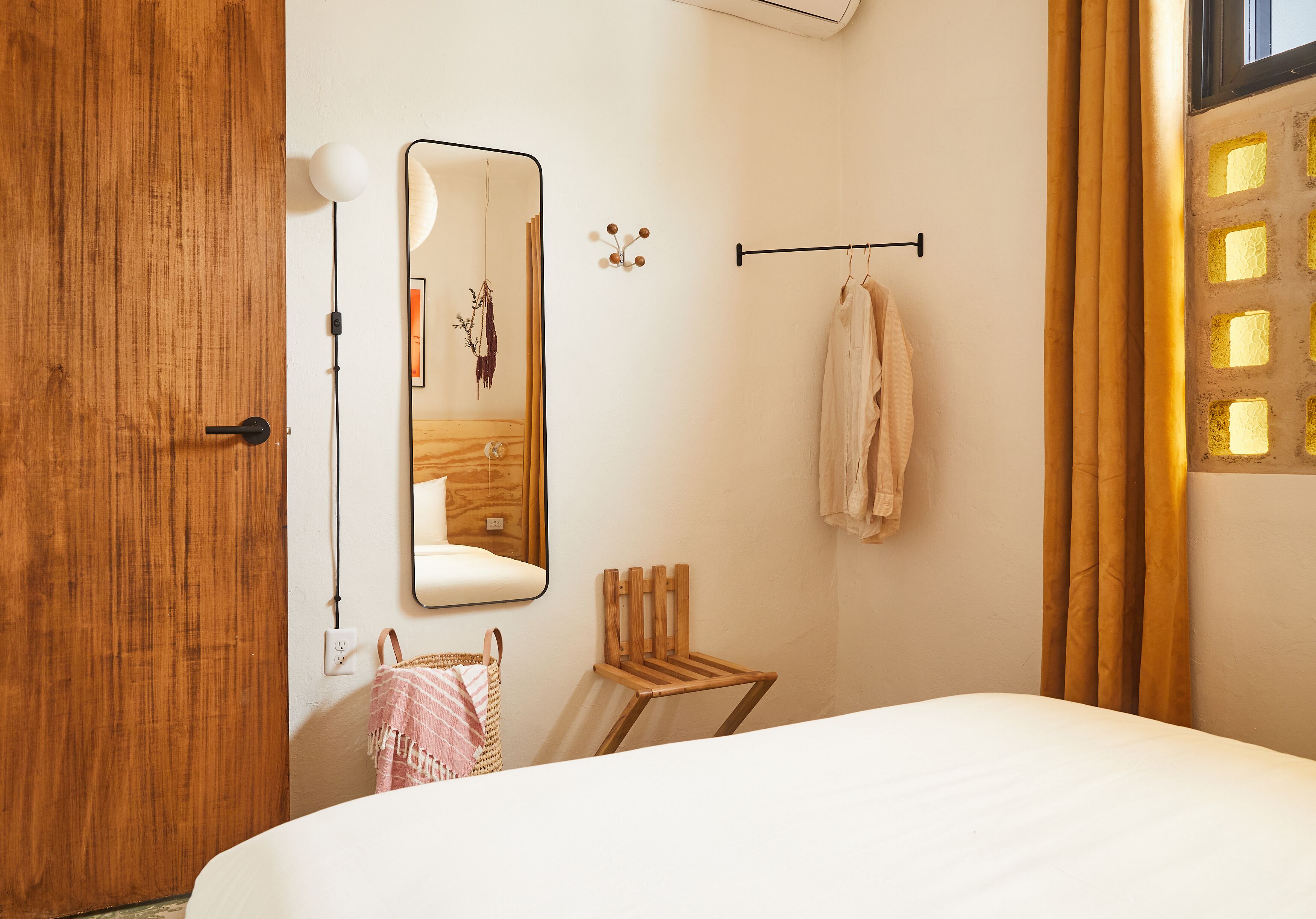 Un dormitorio con puerta de madera, un espejo, toallero colgante, una pequeña silla de madera y una cama.