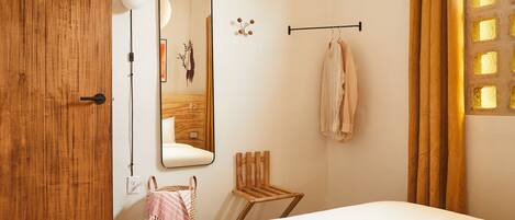 A bedroom with a wooden door, a mirror, a hanging towel rack, a small wooden chair, and a bed.