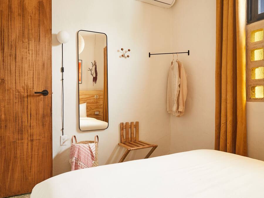 Un dormitorio con puerta de madera, un espejo, toallero colgante, una pequeña silla de madera y una cama.