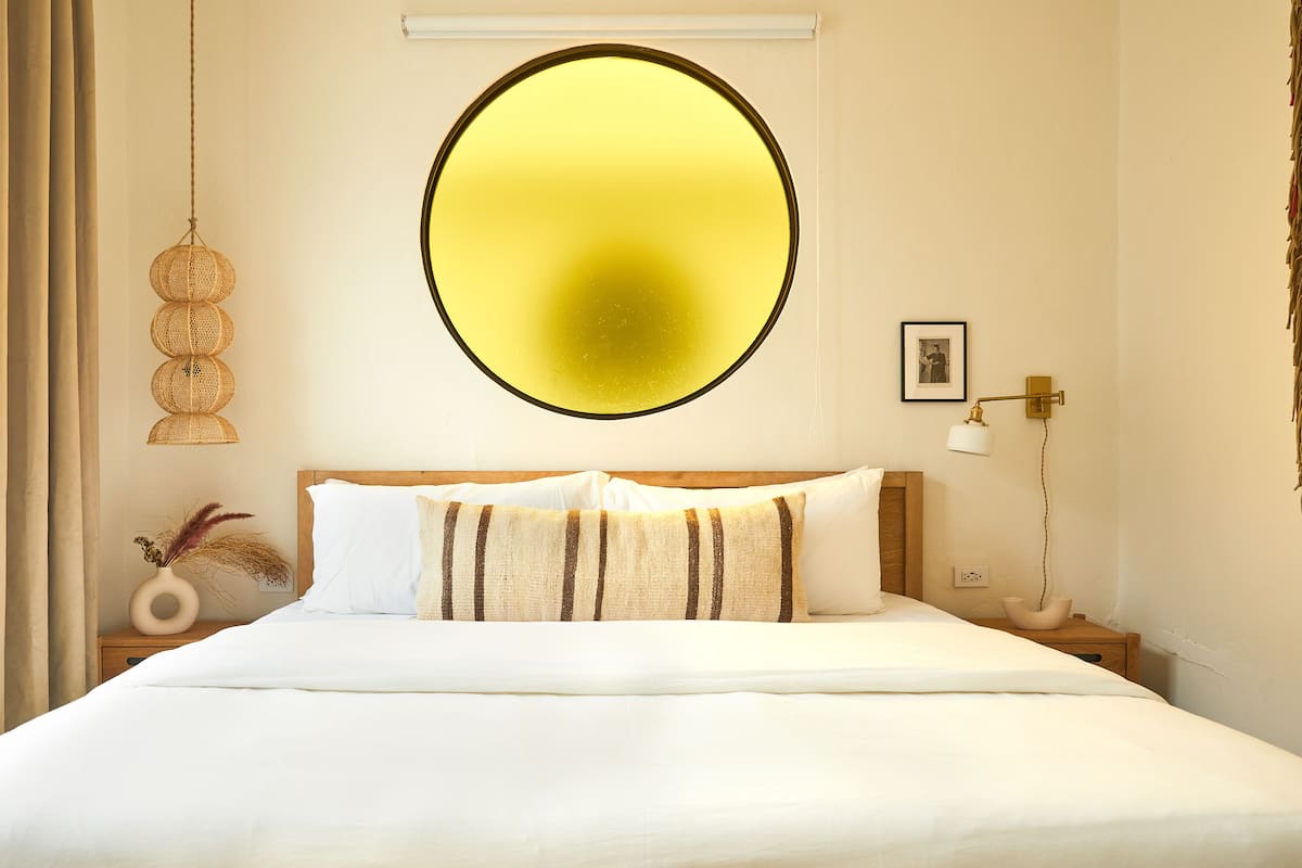 A hotel room with a large bed, a round mirror, a bedside lamp, and a picture on the wall.