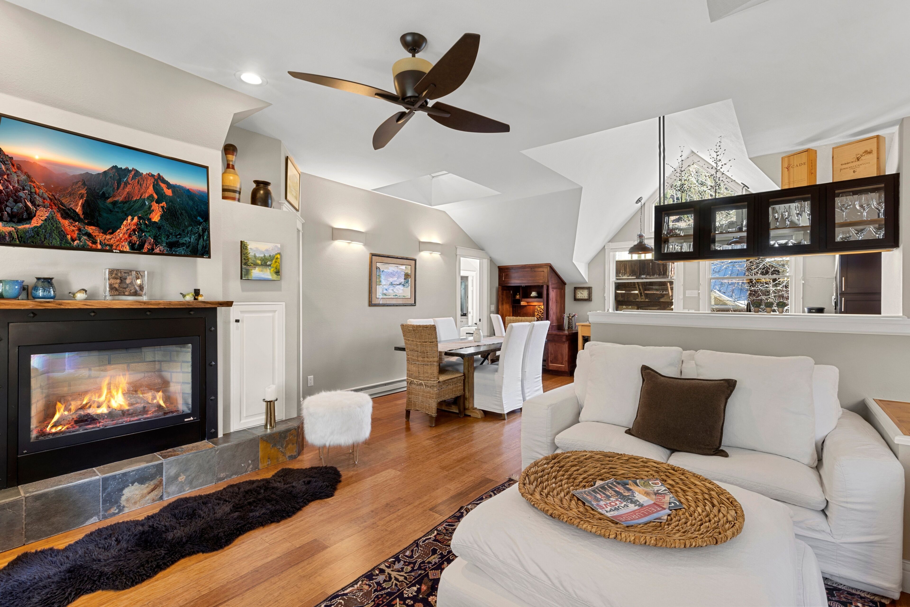 A modern living room with a fireplace, a ceiling fan, and a dining area.