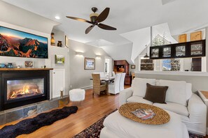 A modern living room with a fireplace, a ceiling fan, and a dining area. - Peaceful Home-like Condo Spacious, Private Deck, Fireplace 3 Bedroom Condo by RedAwning (Telluride)