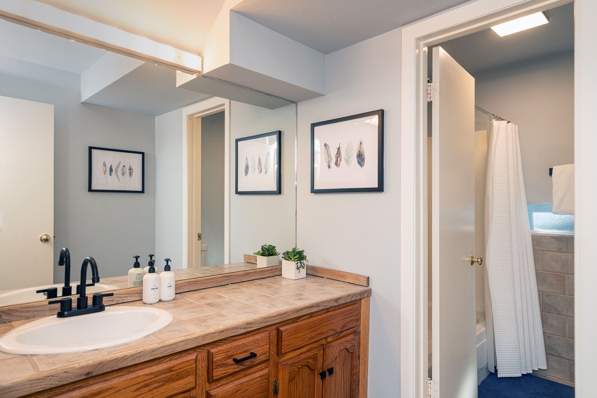 A bathroom with a wooden vanity, a large mirror, framed artwork on the wall, and a shower curtain.