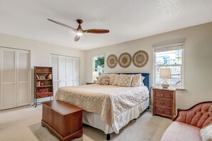 Un dormitorio con cama, cómoda, mesita de noche, mesita auxiliar de mimbre y ventilador de techo.