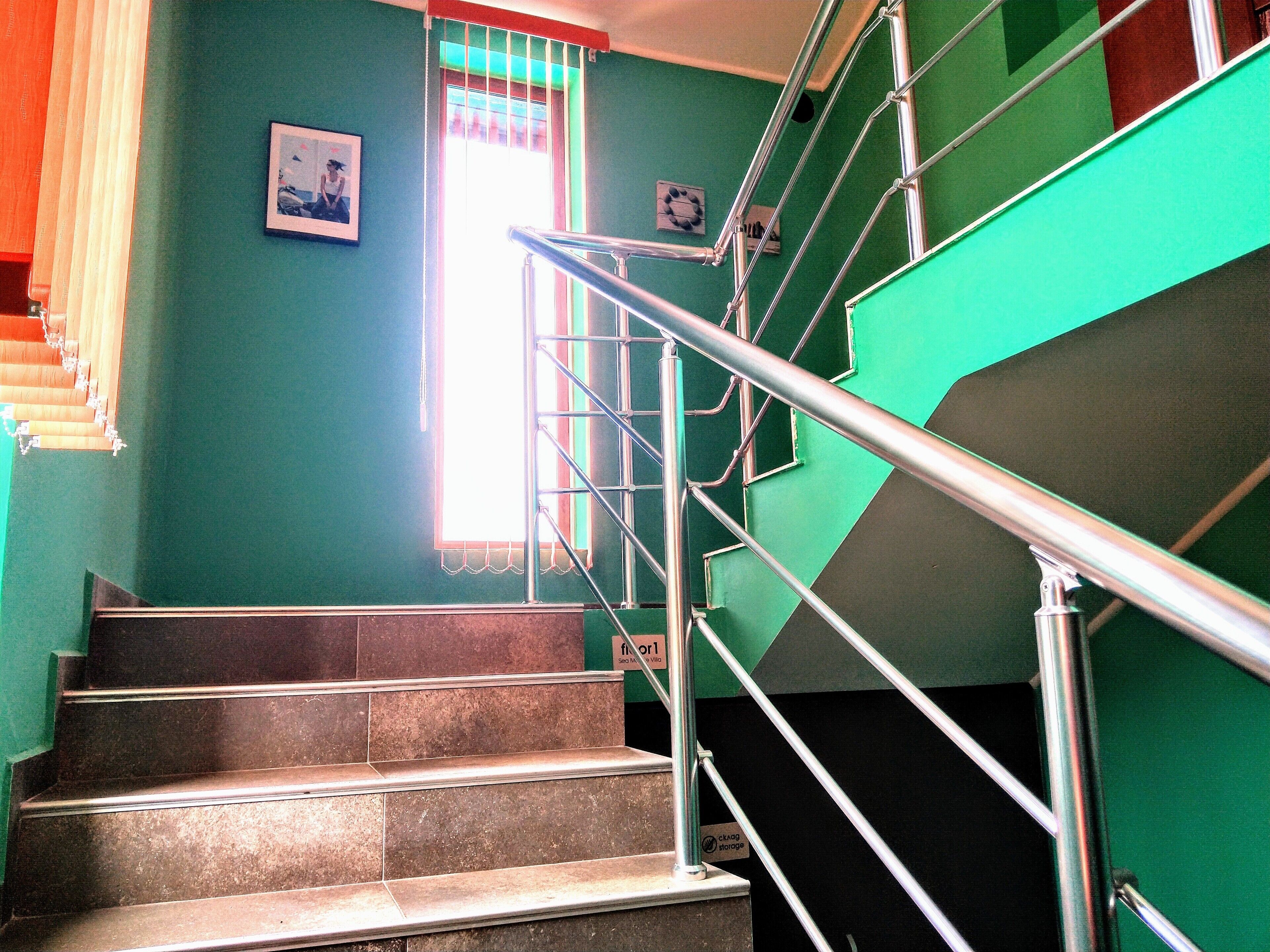 Una escalera con barandillas de metal, una ventana con persianas y un cuadro en la pared.
