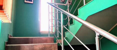 Una escalera con barandillas de metal, una ventana con persianas y un cuadro en la pared.