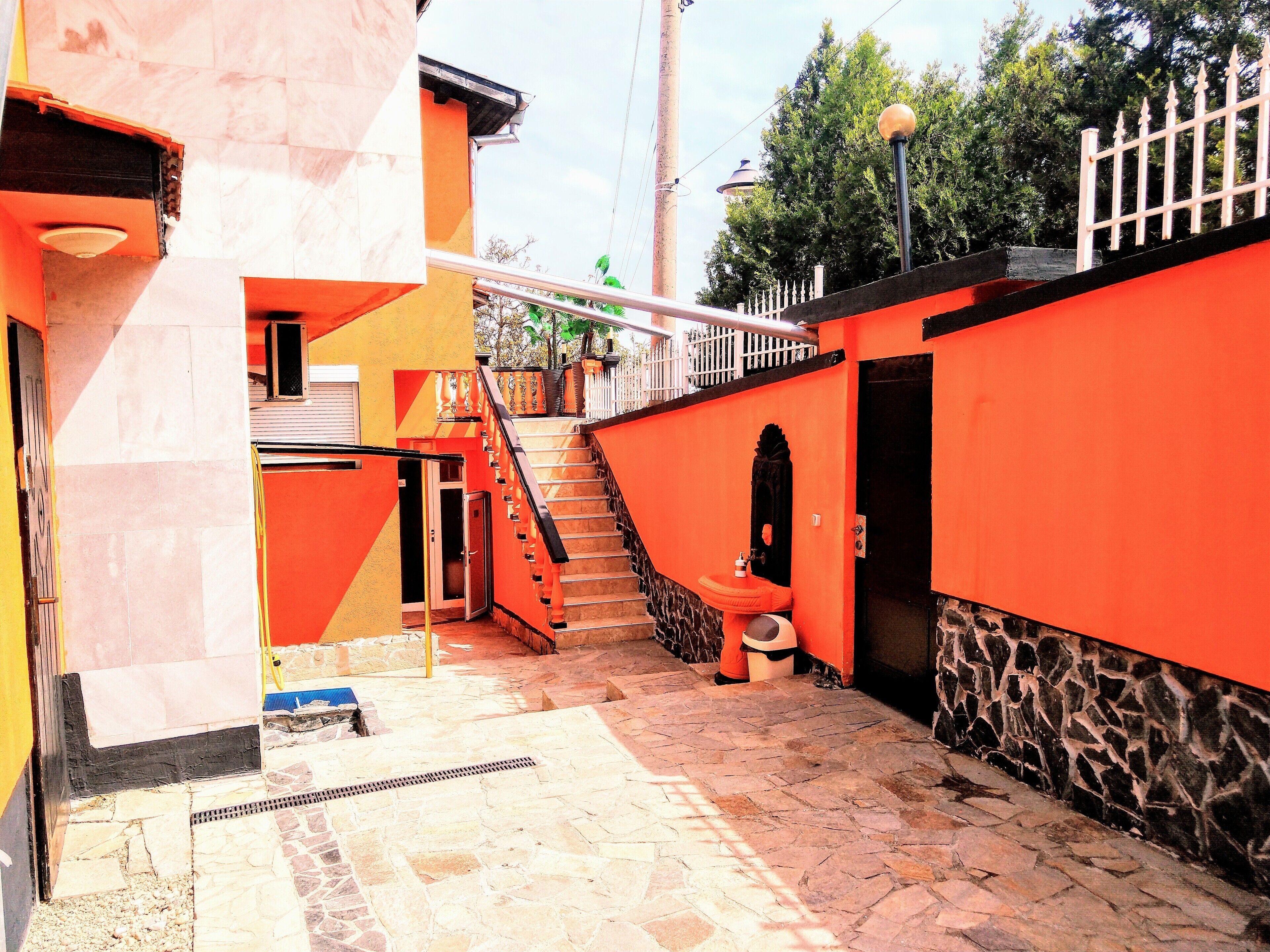 A narrow alleyway with a stone floor, a staircase leading to a second level, and a small outdoor toilet area.